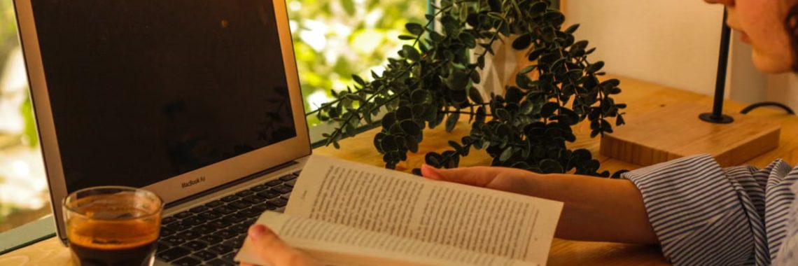 Warm indoor setting with a laptop, coffee, and book creating a cozy workspace.